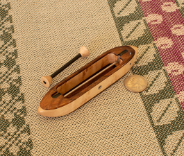 Brocade1 top view 5 1/4" L x 1" W x 13/16" H.  0.9 oz. Walnut featherwood top/bottom and bird's eye maple center. Includes 1 carbonfiber bobbin. Ebony fittings over rod slots; stainless steel rod and yarn hole fitting.